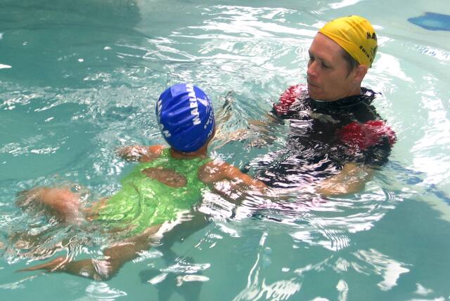 Instructor in a yellow cap teaching a young swimmer