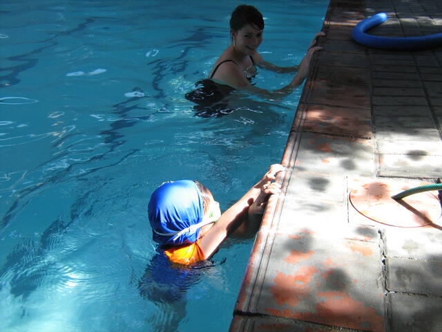 Child in a blue cap at the pool wall